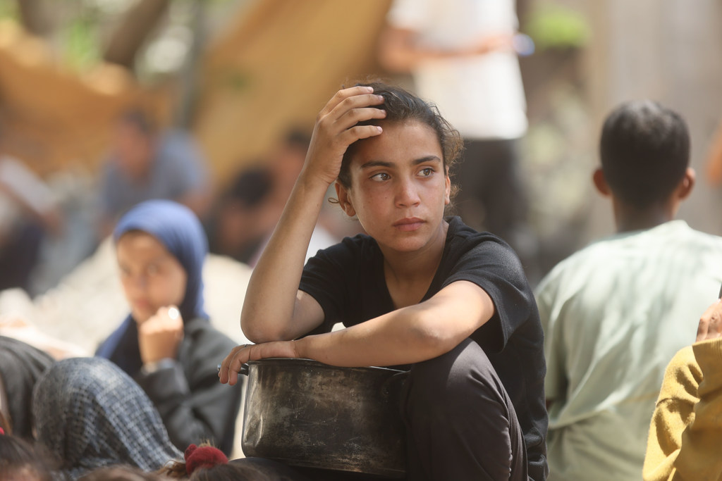 طفلة في غزة تنتظر توزيع الطعام تحت أشعة الشمس الحارقة. عيناها المتعبتان، رغم قوتها الهادئة، تعكسان العبء الذي لا ينبغي لأي طفل أن يتحمله - ألم الجوع، واضطراب الصراع، والشوق إلى حياة بسيطة وهادئة.